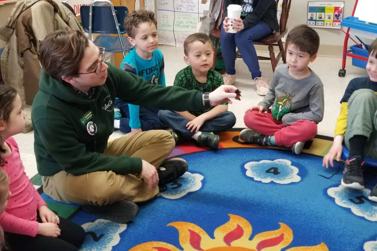 An AmeriCorps member sits on the ground surrounded by children