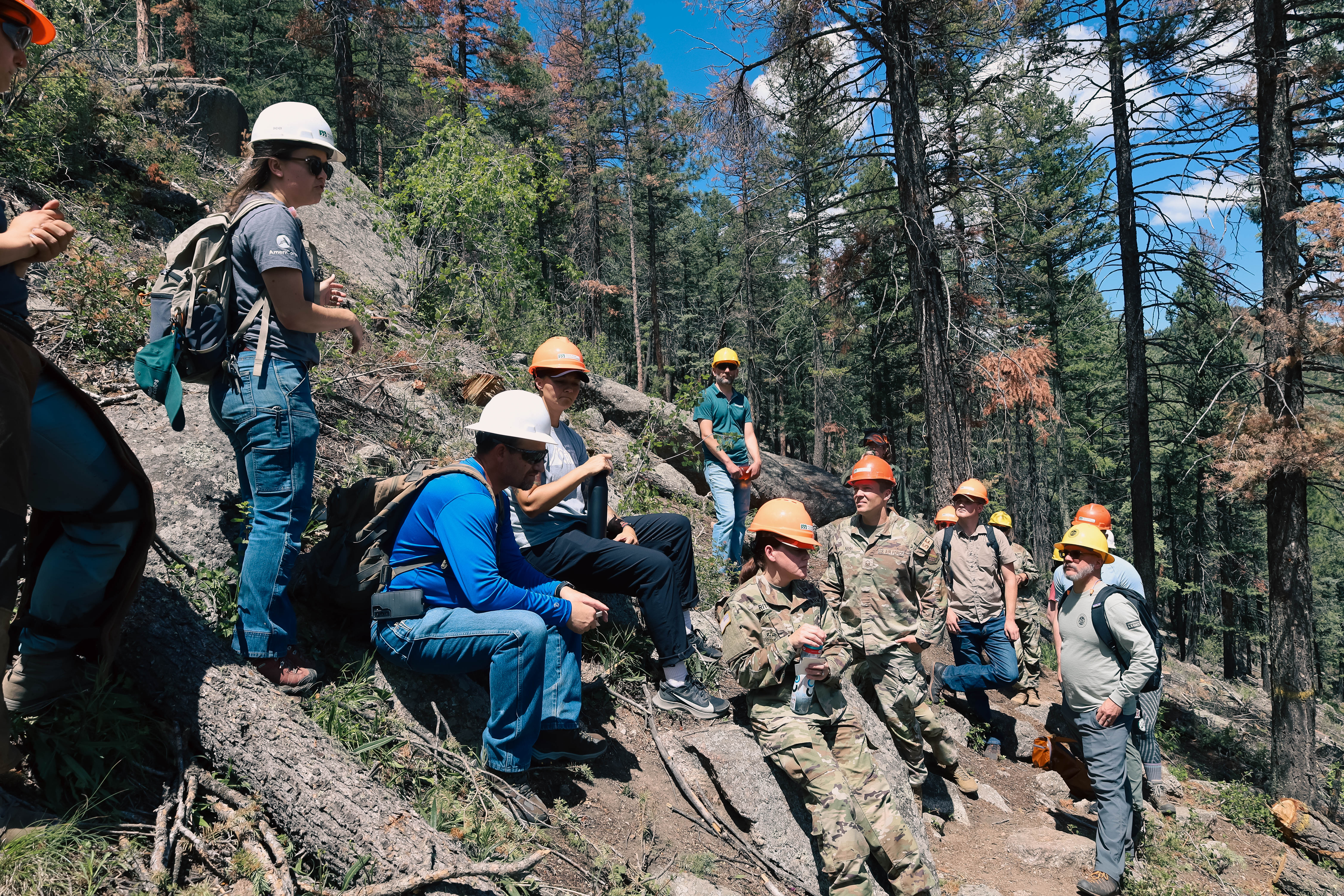 CONG members sit and chat with Mile High Youth Corps members on a trail at a fire mitigation site