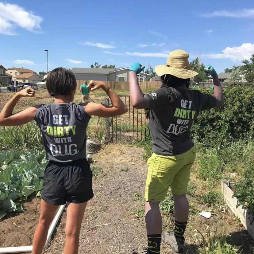 Two AmeriCorps members stand in a garden flexing their muscles