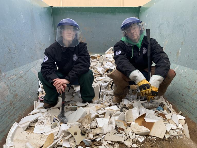 Two members sit on a pile of smashed toilets